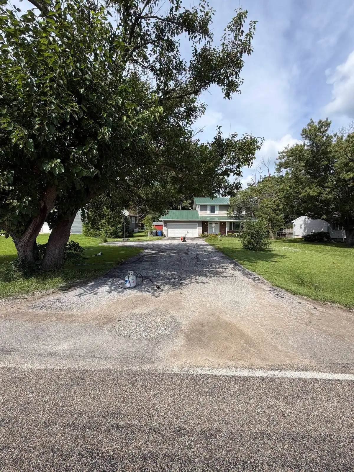 A worn driveway with a loose gravel apron spilling towards the road.
