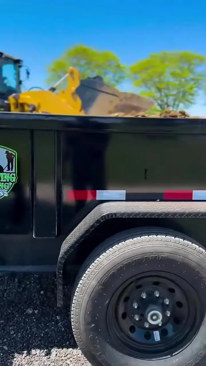 A loader tipping millings into the J&N Paving and Sealcoating dump trailer, the company shield decal visible on the side.
