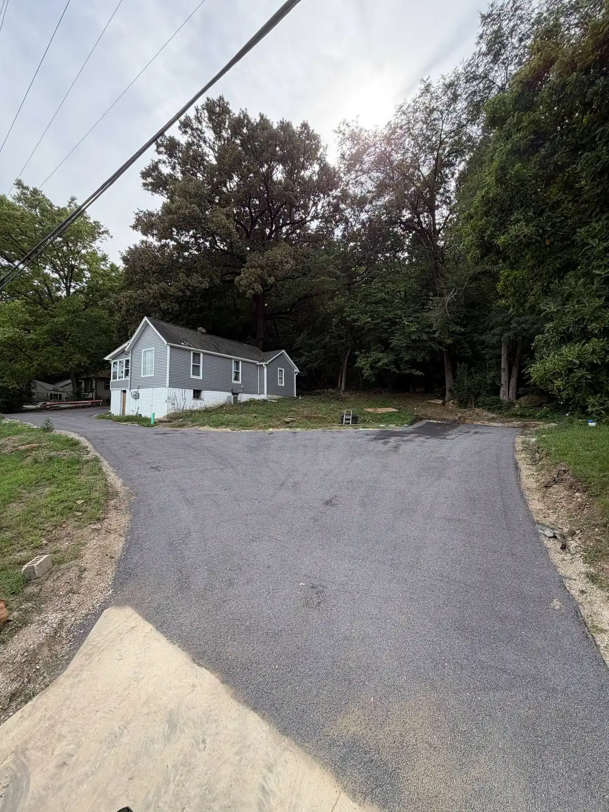 A new tar and chip driveway with a wide turnaround leading to a grey house on a wooded hillside.