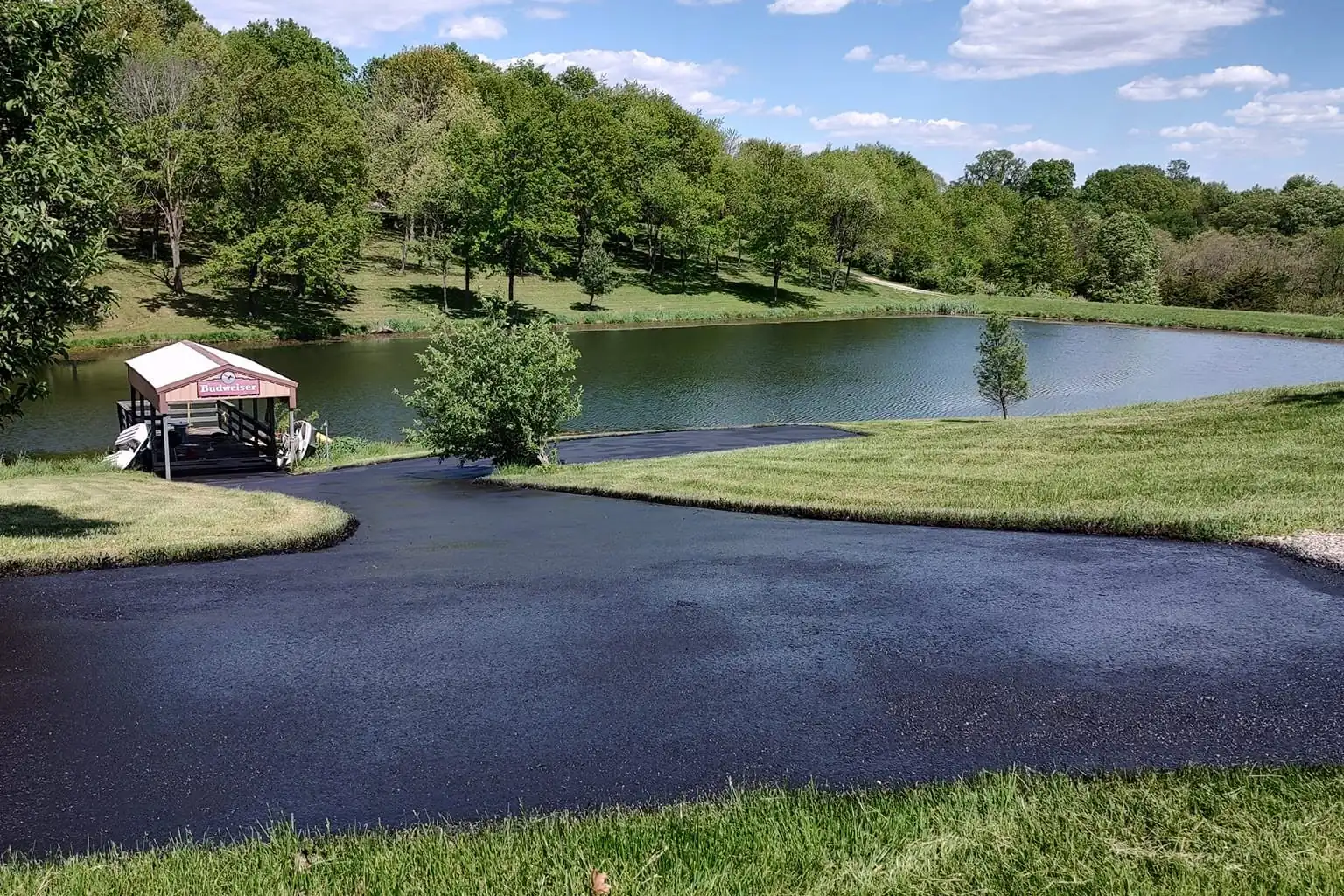 A freshly sealcoated blacktop drive sweeping around a private lake with a boat dock, finished by J&N Paving and Sealcoating.
